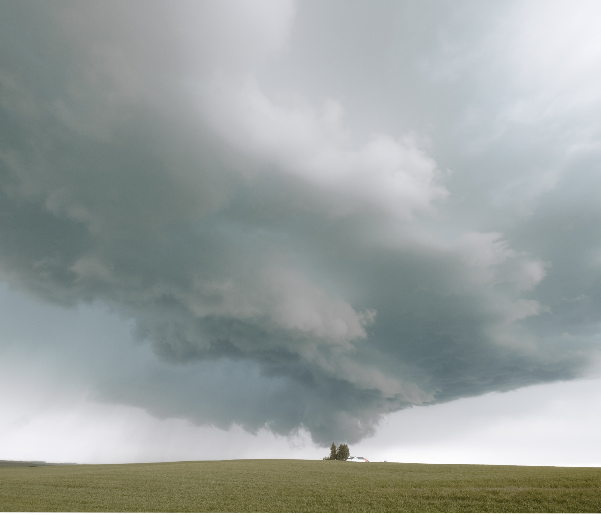 A low storm cloud turning above a small farm on open prairie.