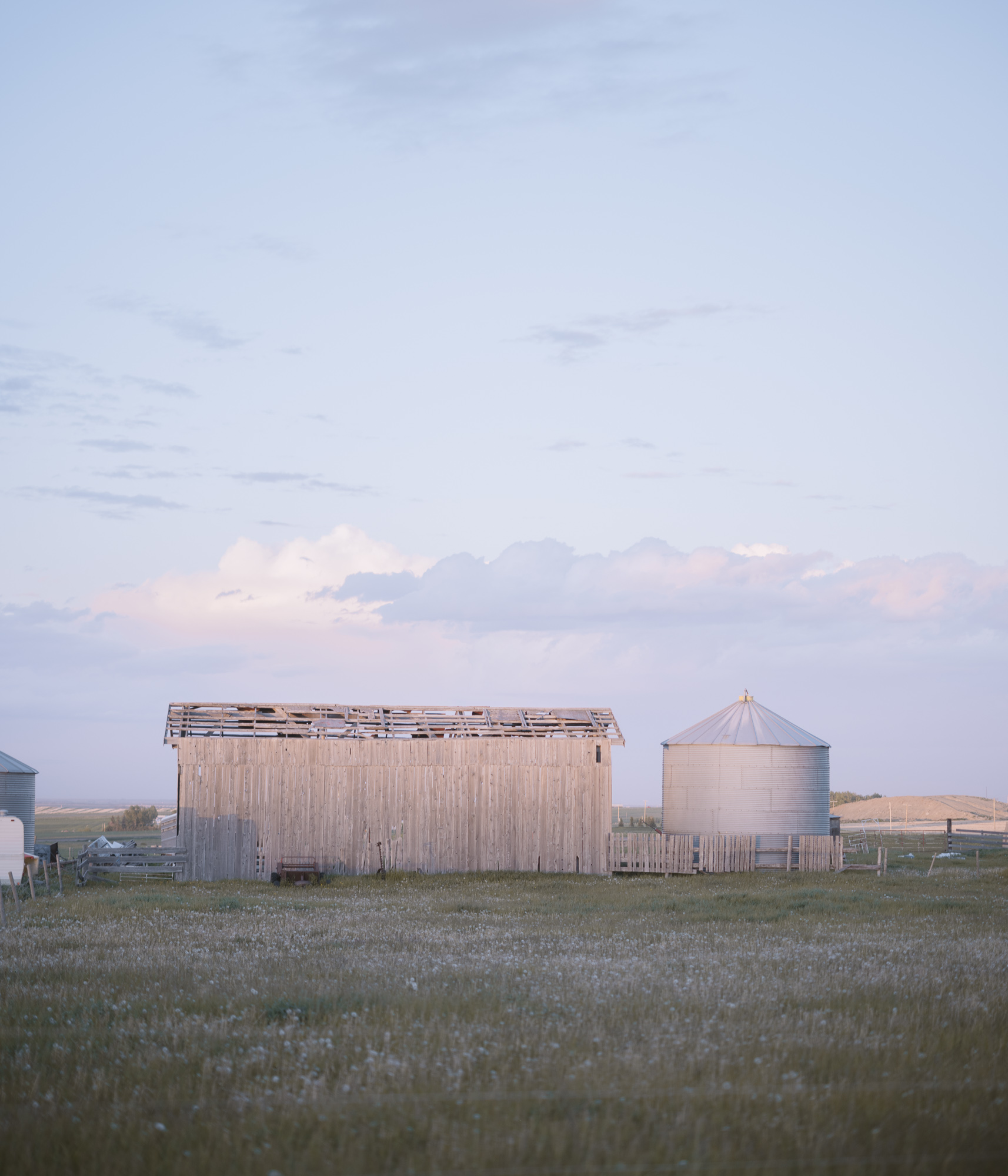 A weathered wooden shed and grain bin beneath a pale evening sky.